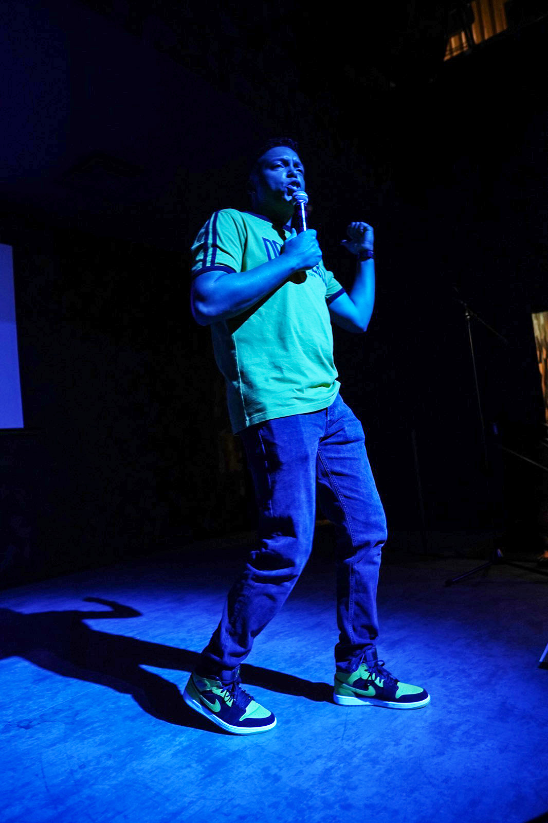 Chris Mayers addressing the room on the microphone under blue and green stage lighting