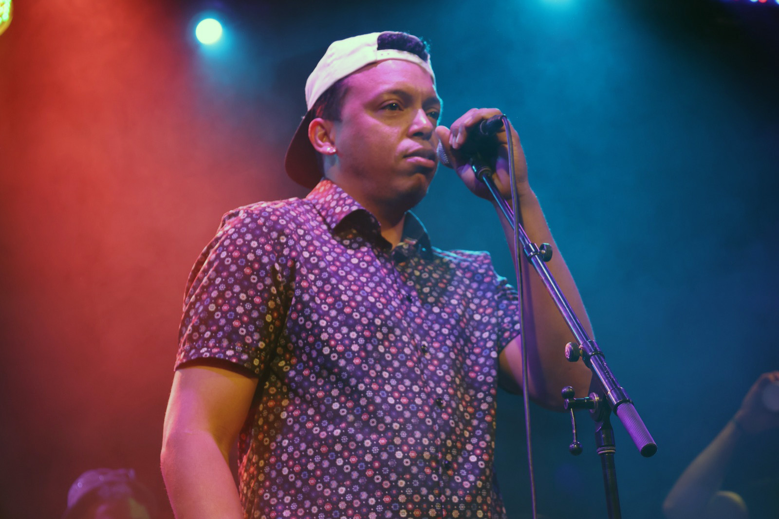 Chris Mayers performing at the microphone under pink and blue stage lighting