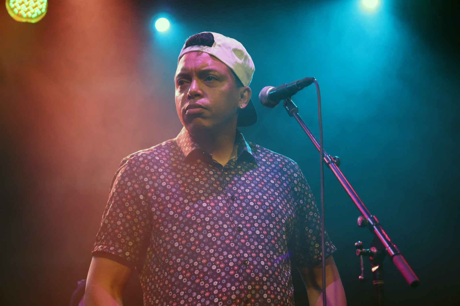 Chris Mayers at the microphone stand mid-performance, stage lights behind him