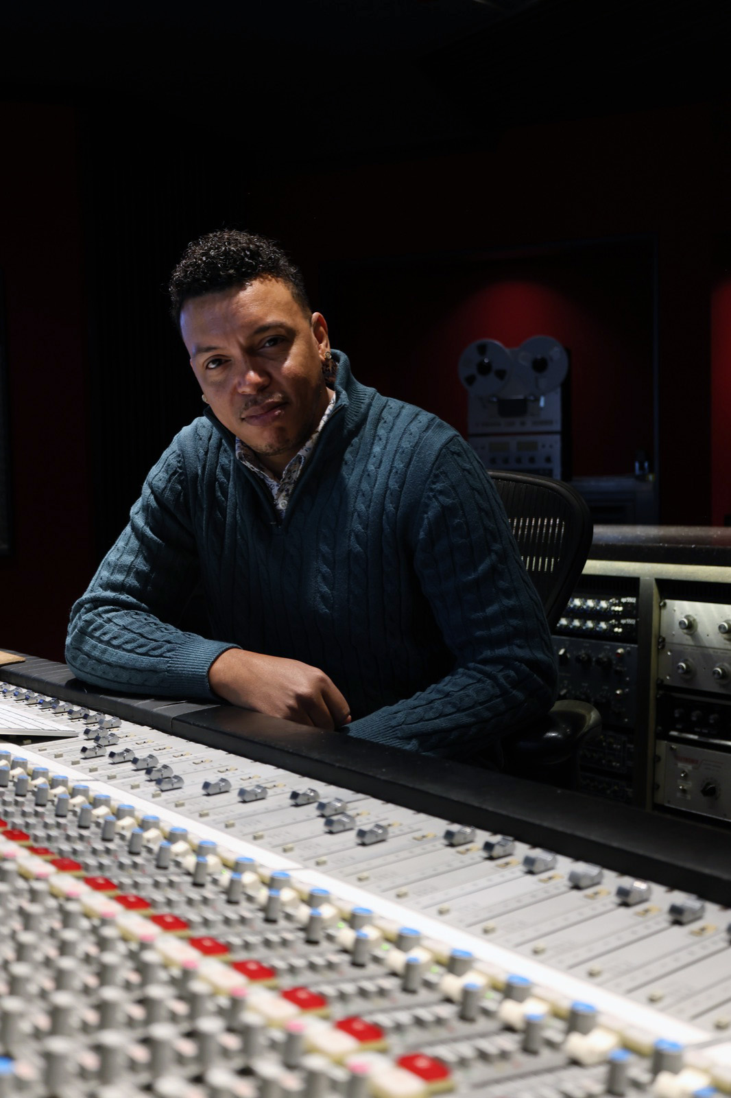 Chris Mayers leaning on a mixing console, tape machine and outboard gear behind him